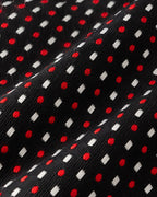 Gros plan du jacquard Tournon : pois rouges et losanges blancs tissés sur une trame noire finement texturée.