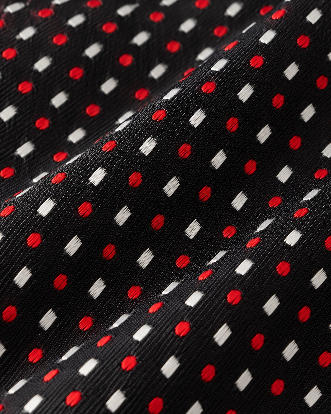 Gros plan du jacquard Tournon : pois rouges et losanges blancs tissés sur une trame noire finement texturée.