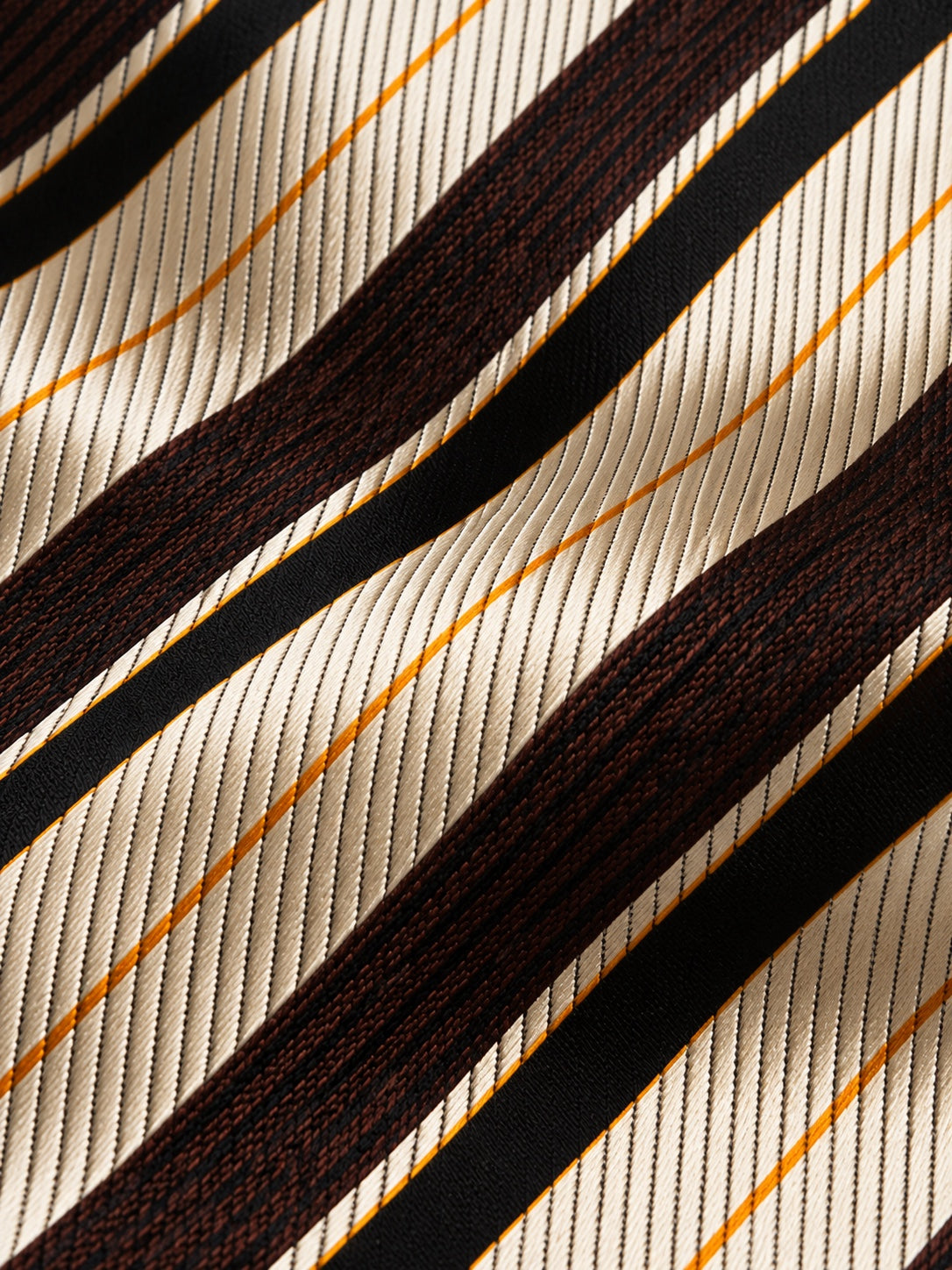 Gros plan du jacquard de soie Tronchet : rayures diagonales ivoire, brun chocolat et noir, avec de fins filets dorés.