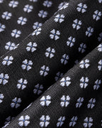 Gros plan du jacquard de soie Valois : petites fleurettes bleu pâle à quatre pétales sur une trame noire.