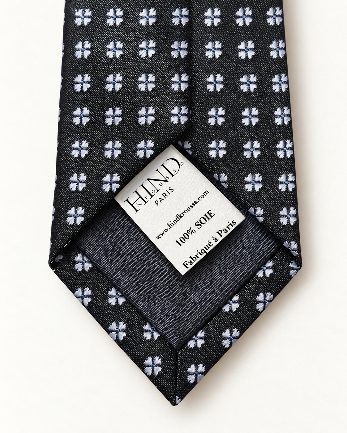 Dos de la cravate Valois noire à fleurettes, doublure sombre et étiquette Hind Kroussa Paris indiquant 100 % soie.
