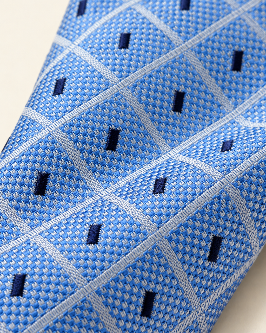 Gros plan du jacquard de soie Vernet : trame bleu ciel, lignes claires entrecroisées et rectangles bleu marine.