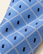 Gros plan du jacquard de soie Vernet : trame bleu ciel, lignes claires entrecroisées et rectangles bleu marine.