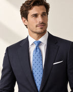 Cravate Vernet bleu ciel à losanges clairs et motifs marine, portée avec un costume sombre et une chemise blanche.