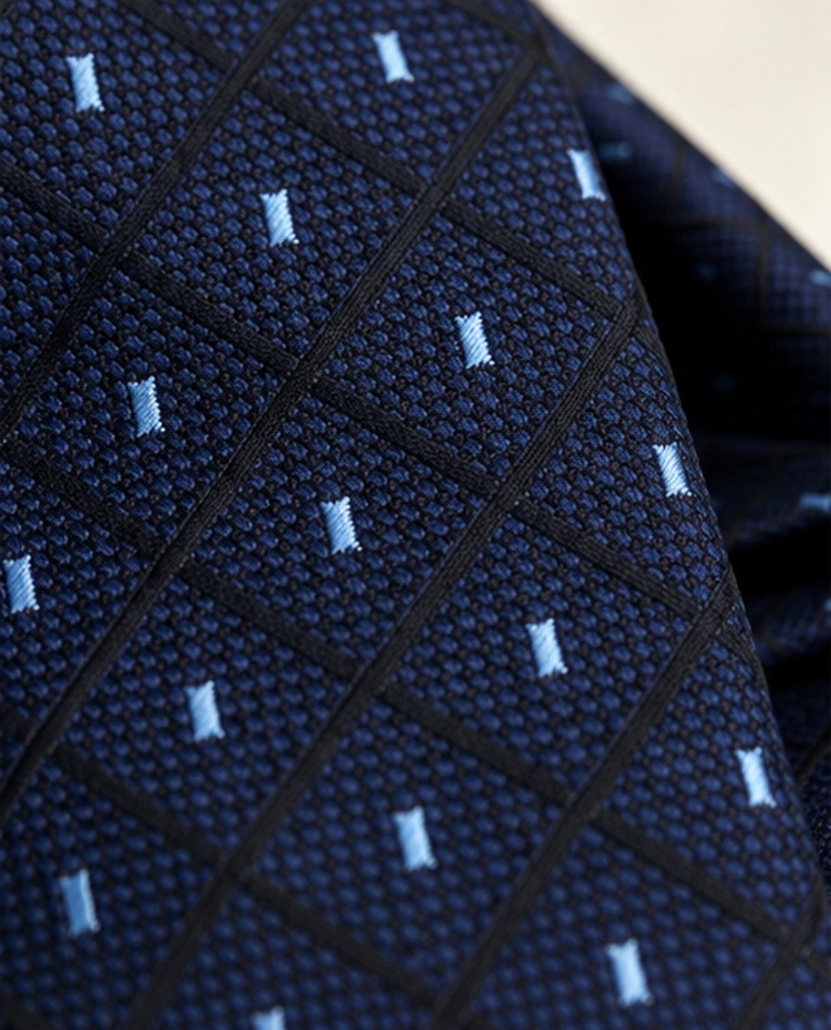 Gros plan du jacquard Vignon : tissage bleu marine texturé, lignes noires en losanges et touches verticales bleu ciel.