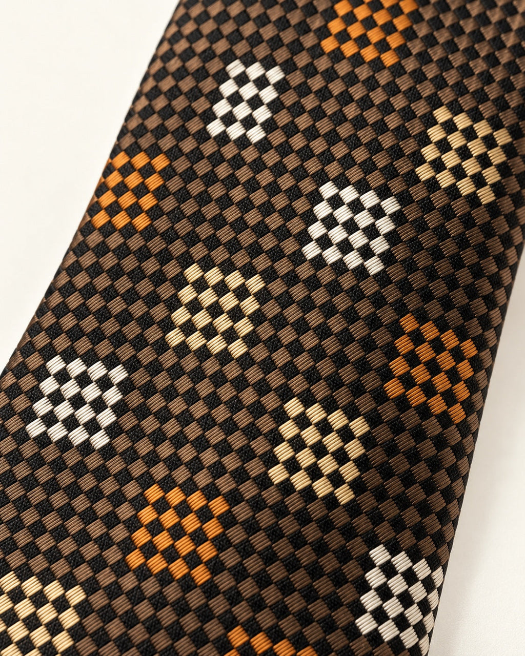 Gros plan du jacquard de soie Volney : petits carreaux bruns et noirs, damiers ivoire, beige et cuivrés.