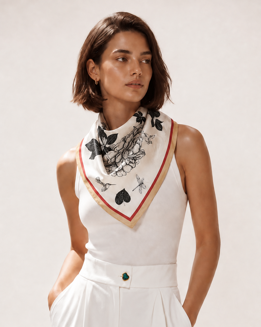 Foulard Rue de Furstemberg en soie ivoire à dessin floral noir et bordure rouge et dorée, porté avec une tenue blanche.