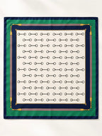 Foulard carré Rue de l’Éperon à plat, motif de mors noirs sur ivoire, encadré de bandes vert émeraude et bleu marine avec ornements dorés et roses.