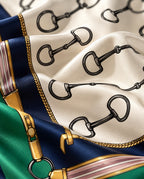Zoom matière du foulard Rue de l’Éperon : mors noirs sur soie ivoire, détails dorés, rubans roses, bordure verte et bleu marine.