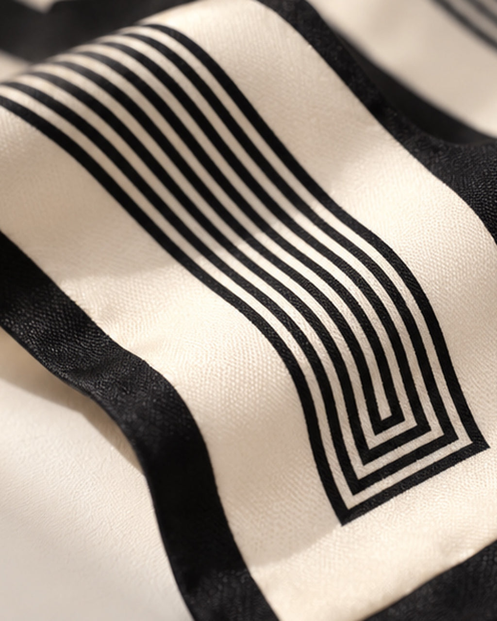 Zoom sur le foulard Rue de l’Odéon en soie ivoire : lignes noires parallèles et géométriques encadrées d’une bordure noire.