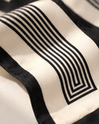 Zoom sur le foulard Rue de l’Odéon en soie ivoire : lignes noires parallèles et géométriques encadrées d’une bordure noire.