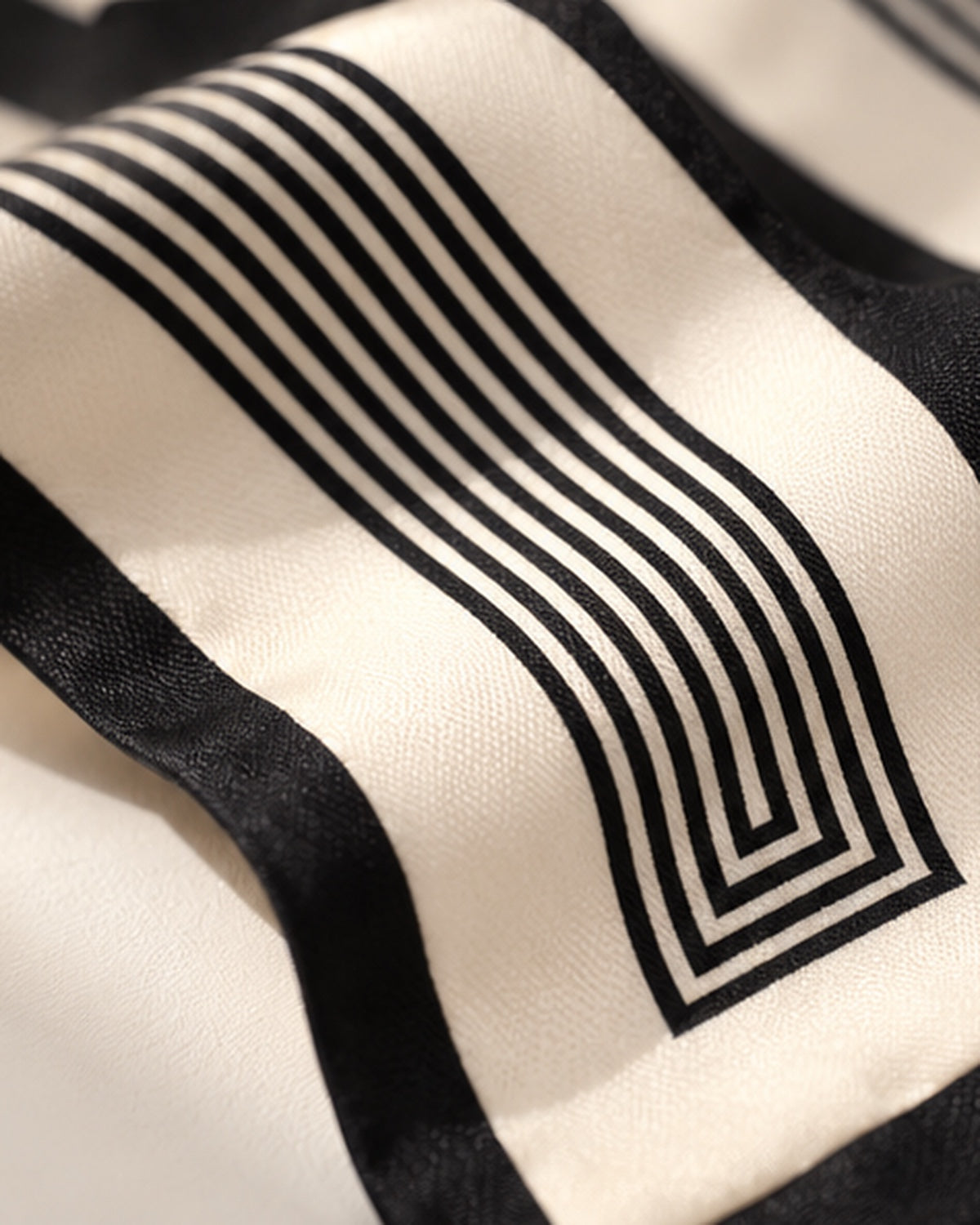 Zoom sur le foulard Rue de l’Odéon en soie ivoire : lignes noires parallèles et géométriques encadrées d’une bordure noire.