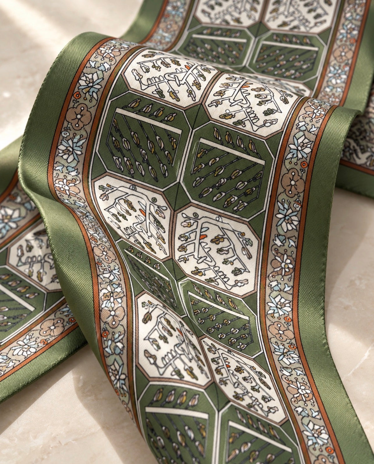 Détail du foulard Rue de la Paix en soie : médaillons verts et ivoire à motifs végétaux, encadrés de frises brunes.