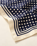 Zoom sur le foulard Rue de Tournon en soie : pois ivoire sur bleu marine et bordure crème à rayures marines.