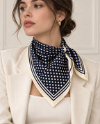 Foulard Rue de Tournon en soie bleu marine à pois ivoire, noué au cou sur un blazer écru.