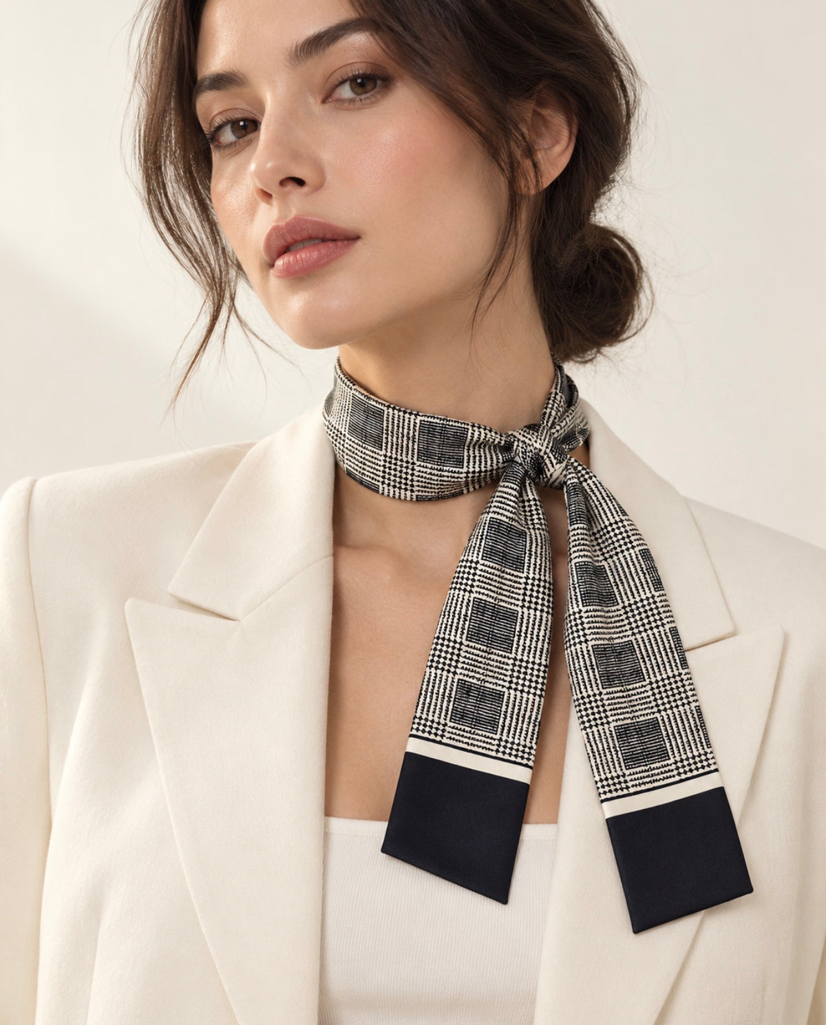 Foulard long Rue de Verneuil en soie à carreaux noirs et ivoire, noué au cou d’un mannequin avec un blazer crème.